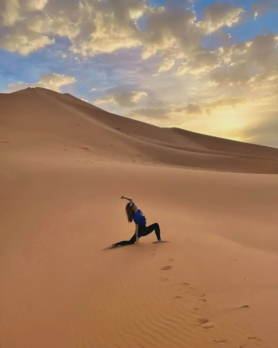 Woman practicing yoga on golden sand dunes during sunset in the Moroccan Sahara Desert