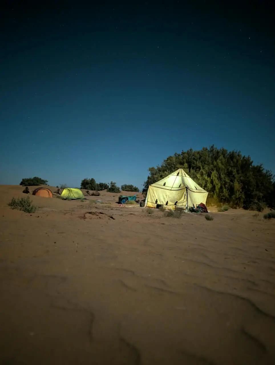 A brightly illuminated tent stands in a desert camp at night.