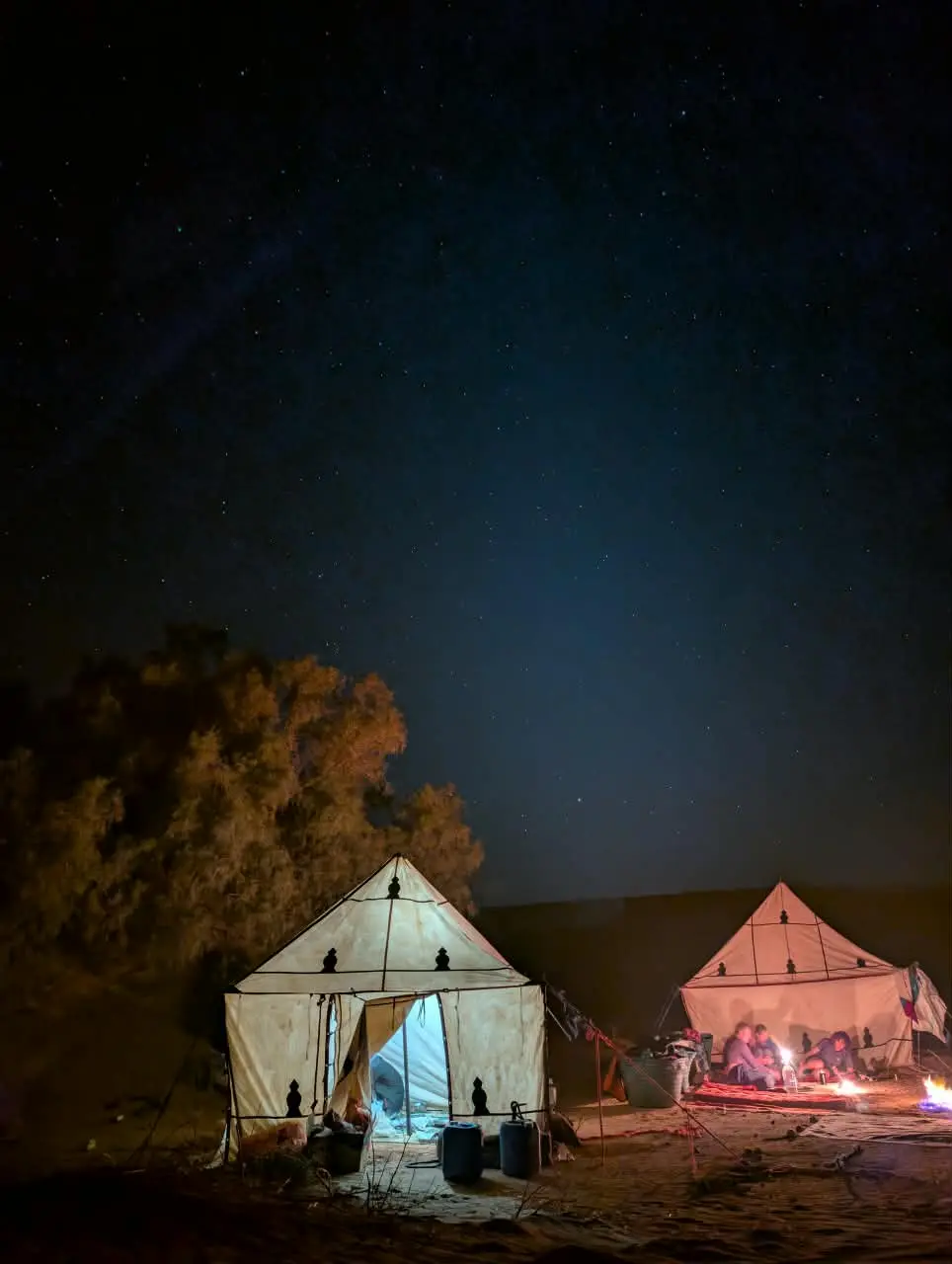 Two illuminated tents glow at a desert camp beneath a dark starry sky.